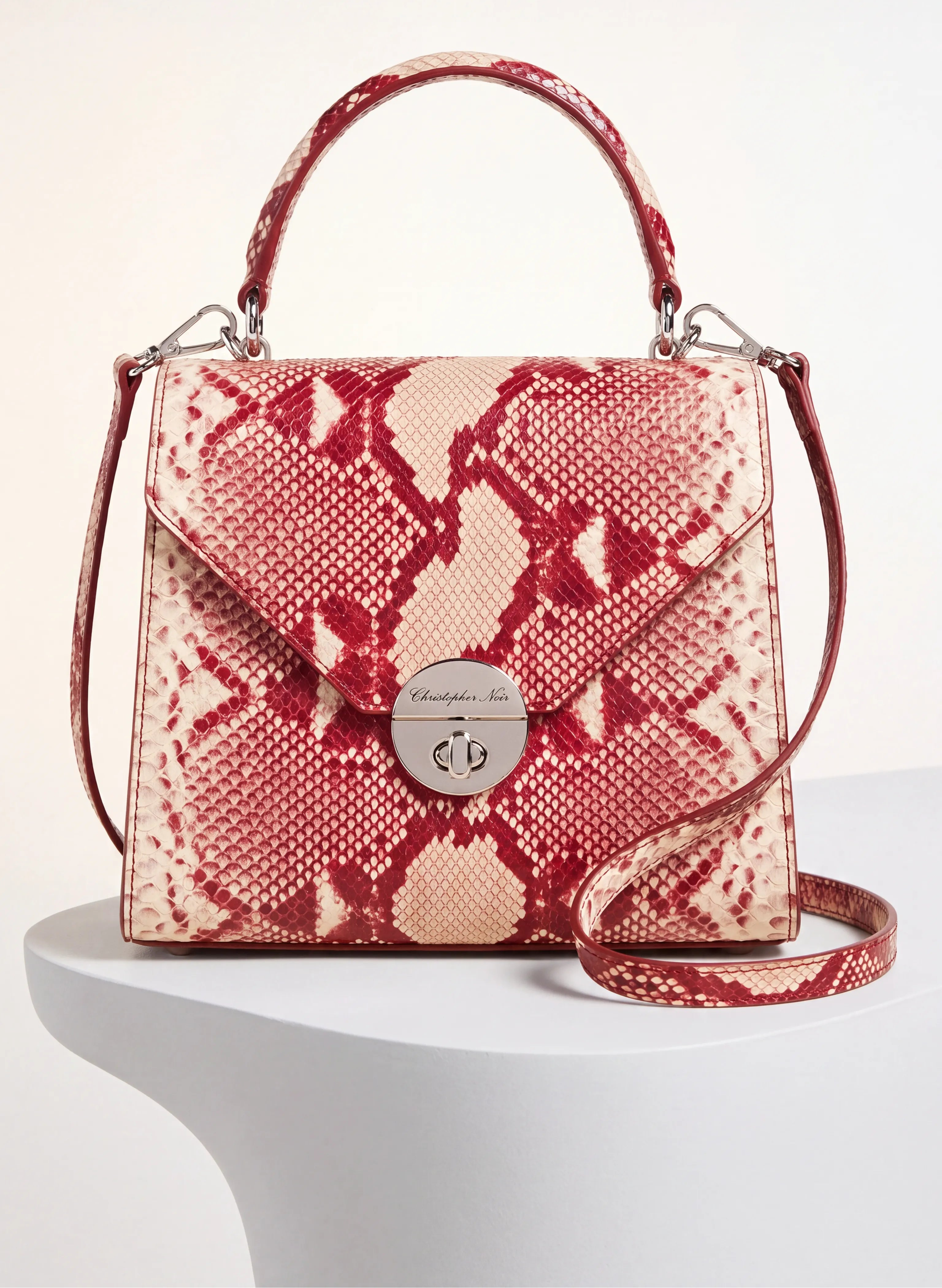 A Salvatore Ferragamo snakeskin-patterned handbag in red and beige, displayed on a white pedestal against a light beige background.