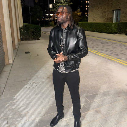 Man in a black leather jacket standing on a sidewalk at night.
