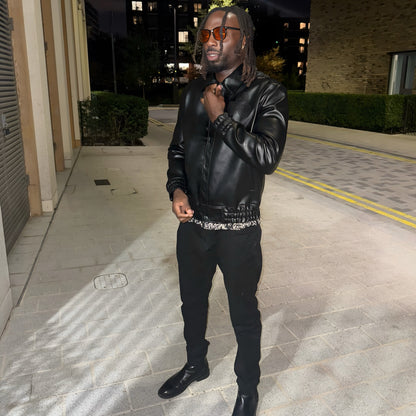 Man in a black leather jacket standing on a street at night.