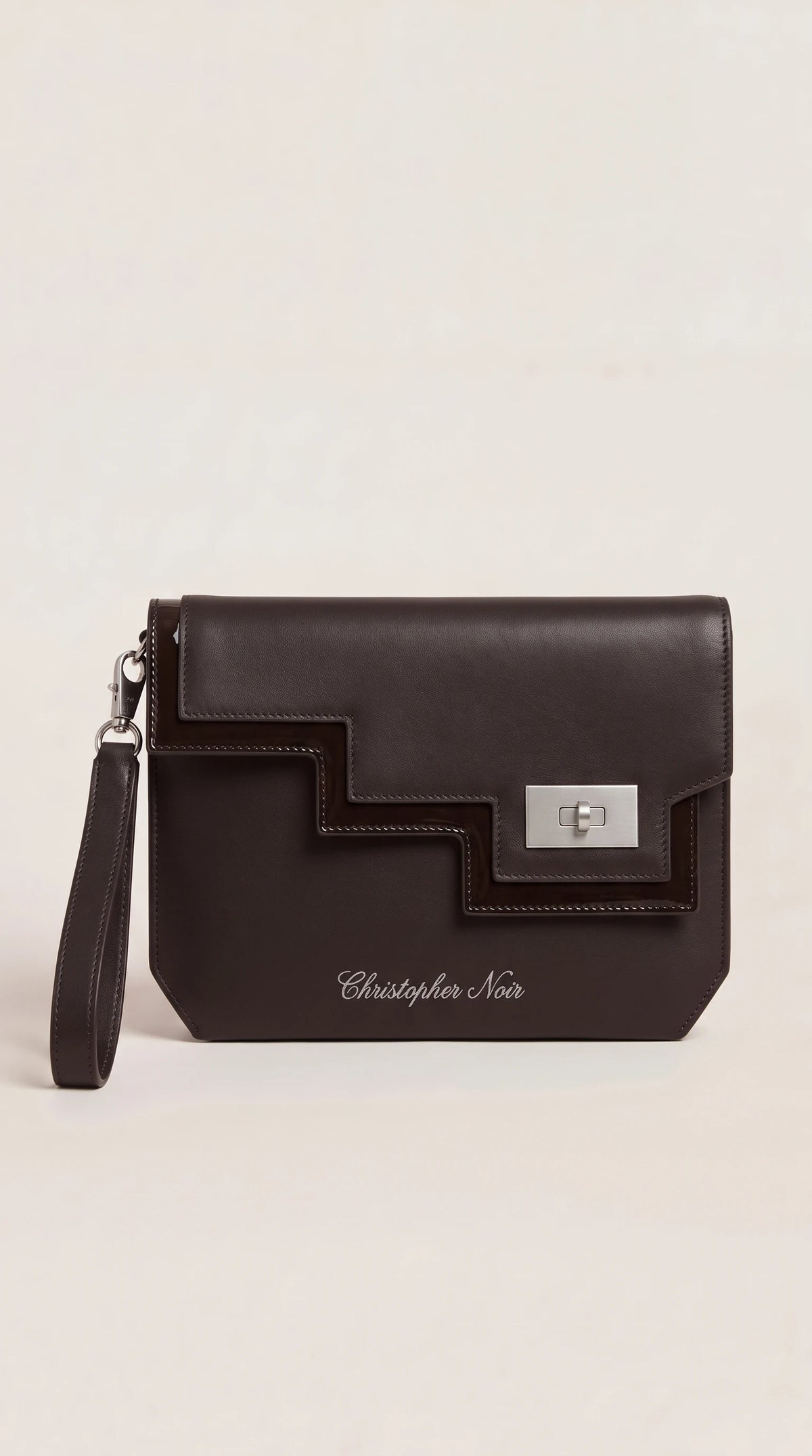The Noir Rothbury dark brown leather wristlet clutch, front view with stepped geometric panel and silver-tone turn-lock