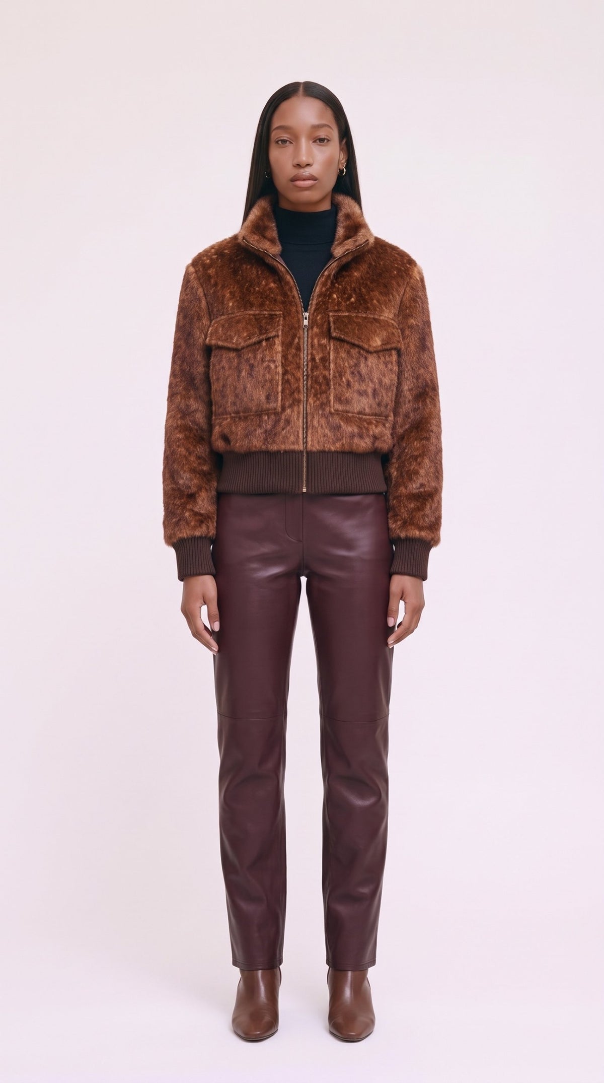 Model wearing the rust faux-fur bomber with a black roll-neck and burgundy leather trousers