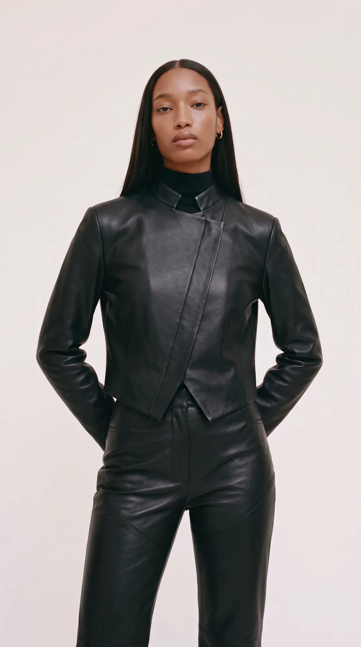 The Noir Wyre cropped black leather jacket with notched stand collar and diagonal wrap front ending in a pointed hem
